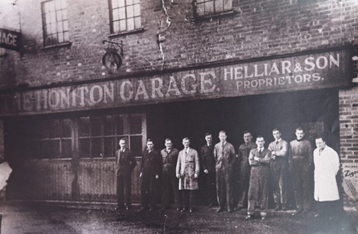 Black and white photograph of the staff lined up beneath the sign The Honiton Garage, Helliar and Son Proprietors