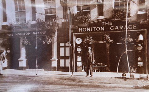 Sepia photograph of The Honiton Garage frontage with hand-operated fuel pumps on the pavement