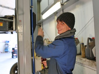 Mechanic in a beanie hat at the vehicle lift controls