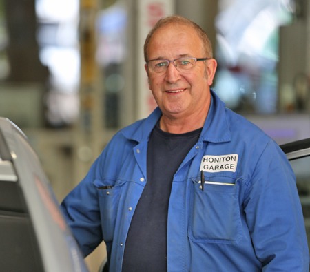 Senior mechanic in blue Honiton Garage overalls smiling in the workshop
