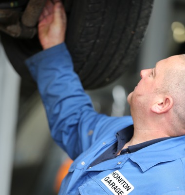 Mechanic in Honiton Garage overalls working under a raised car