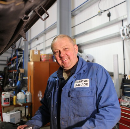 Mechanic in Honiton Garage overalls at the workbench with tool chests behind