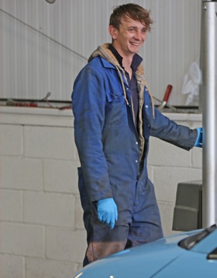 Young mechanic in overalls and gloves smiling in the MOT bay