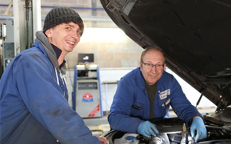 Two mechanics smiling under a raised bonnet