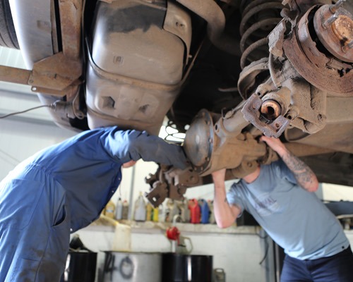 Two people working on a car's suspension from underneath