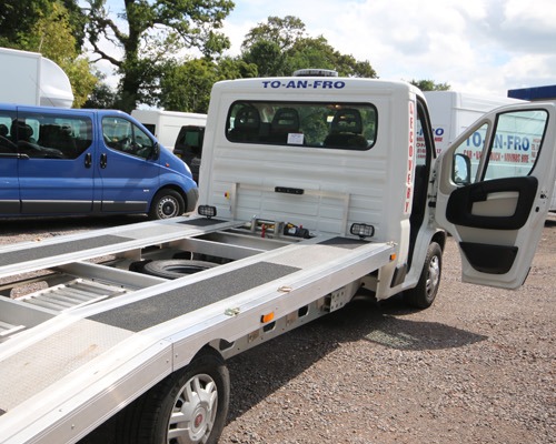 White beaver-tail recovery truck lettered To-An-Fro Recovery, ramp ready on the yard